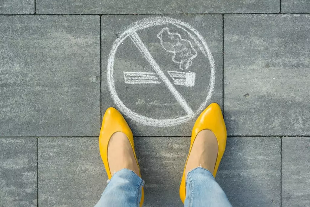 Female feet with picture no smoking painted on the grey sidewalk