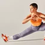 self-esteem, body positivity, flexible and short haired woman stretching legs on grey background,